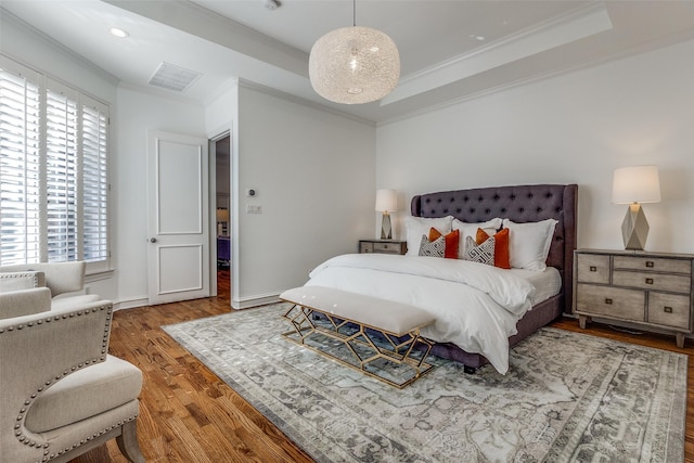 bedroom with hardwood / wood-style flooring, a tray ceiling, and crown molding