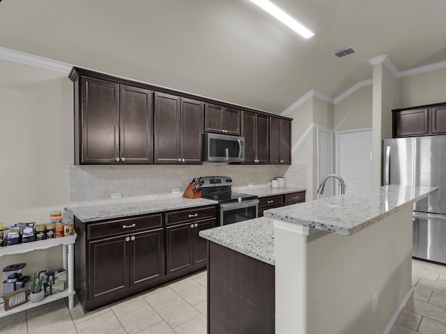 kitchen with appliances with stainless steel finishes, a kitchen island with sink, light tile patterned floors, dark brown cabinetry, and light stone countertops