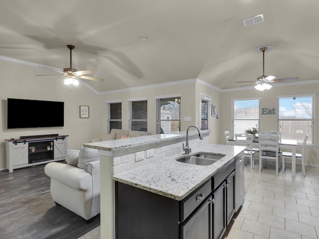 kitchen featuring lofted ceiling, sink, dishwasher, light stone countertops, and a center island with sink