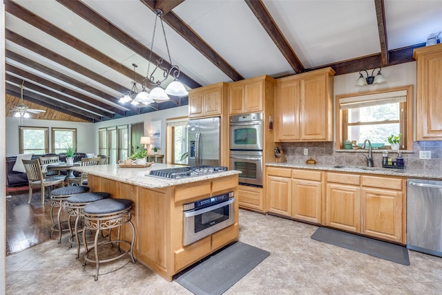 kitchen with a center island, vaulted ceiling with beams, hanging light fixtures, appliances with stainless steel finishes, and plenty of natural light