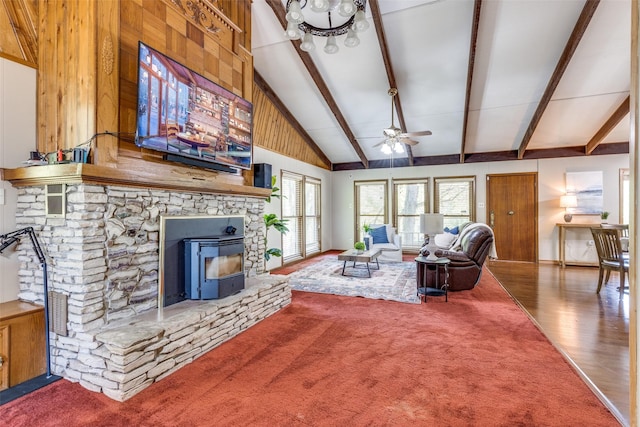 carpeted living room with ceiling fan, beamed ceiling, and a wood stove