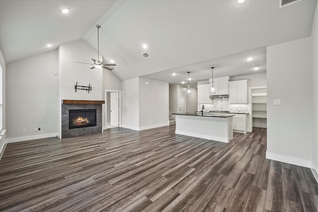 unfurnished living room with dark hardwood / wood-style flooring, sink, high vaulted ceiling, ceiling fan, and a tiled fireplace