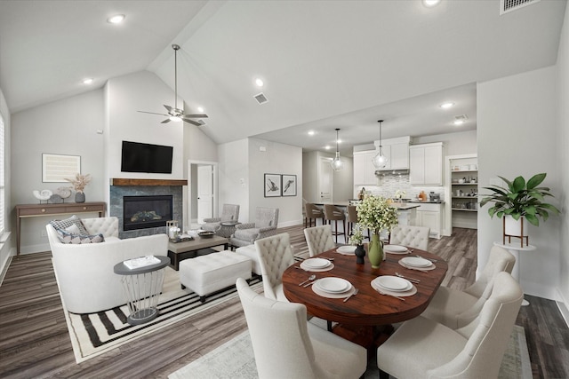 dining room with ceiling fan, a fireplace, dark hardwood / wood-style floors, and high vaulted ceiling