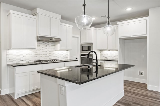 kitchen with an island with sink, stainless steel appliances, decorative light fixtures, white cabinets, and sink