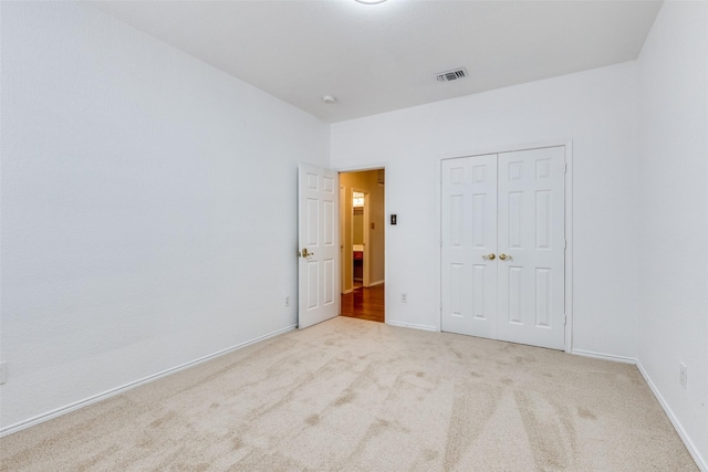 unfurnished bedroom featuring baseboards, a closet, visible vents, and light colored carpet