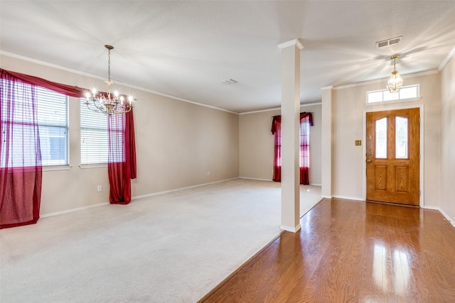 carpeted entryway featuring decorative columns, visible vents, wood finished floors, crown molding, and a notable chandelier