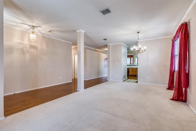 carpeted spare room with decorative columns, visible vents, a chandelier, and ornamental molding