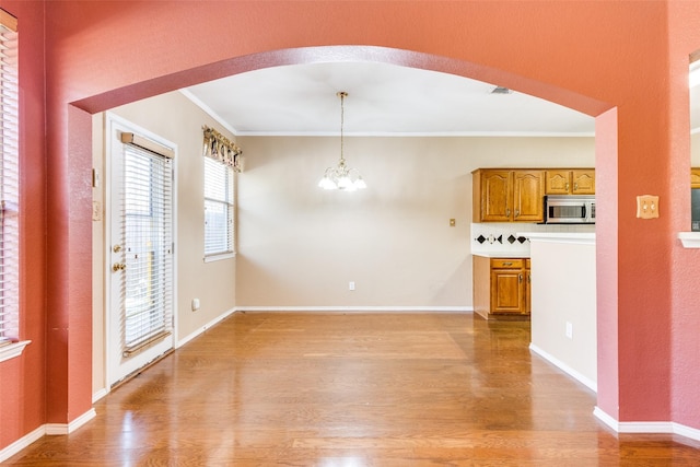 interior space with arched walkways, ornamental molding, a notable chandelier, and light wood-style floors