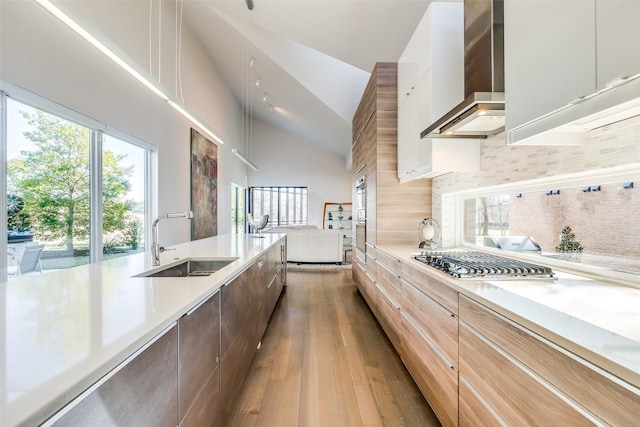 kitchen featuring lofted ceiling, wall chimney range hood, sink, backsplash, and stainless steel gas cooktop