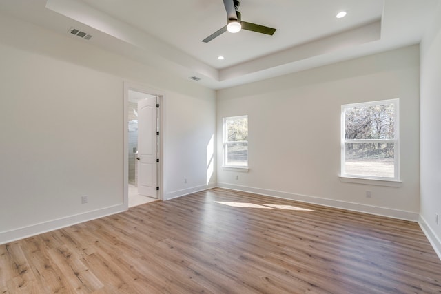 unfurnished room with ceiling fan, light wood-type flooring, and a tray ceiling