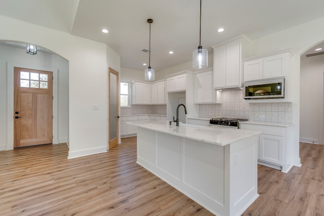 kitchen with stove, pendant lighting, white cabinets, and a kitchen island with sink