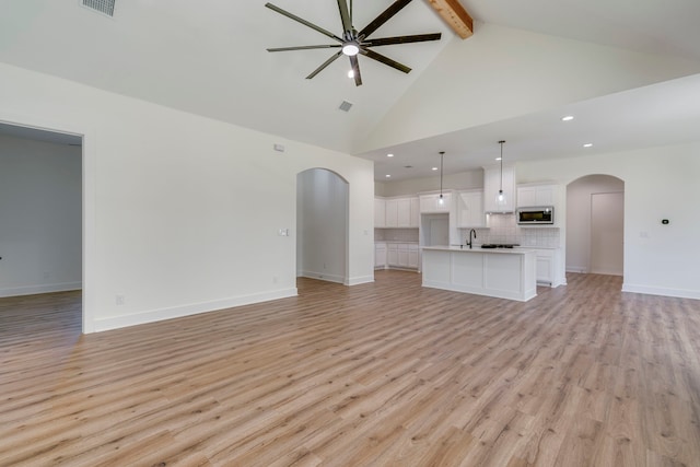 unfurnished living room with light hardwood / wood-style floors, ceiling fan, beamed ceiling, high vaulted ceiling, and sink