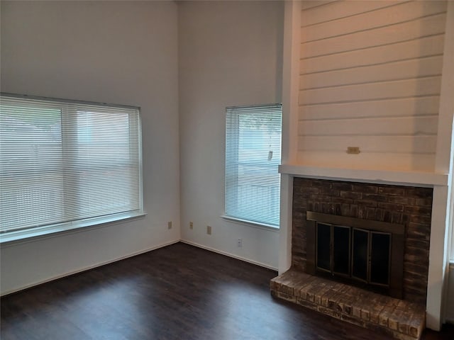 unfurnished living room with dark wood-type flooring and a brick fireplace