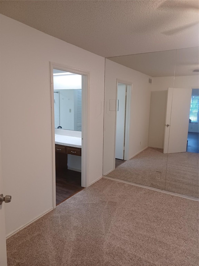 unfurnished bedroom with dark carpet, ensuite bathroom, a closet, and a textured ceiling