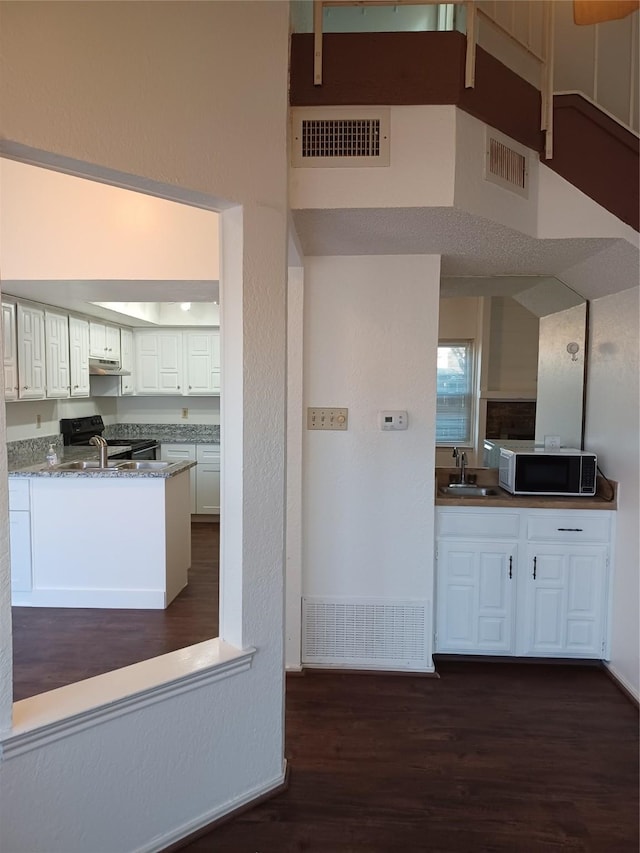 kitchen featuring white cabinets, dark hardwood / wood-style flooring, dark stone counters, black range with electric cooktop, and sink