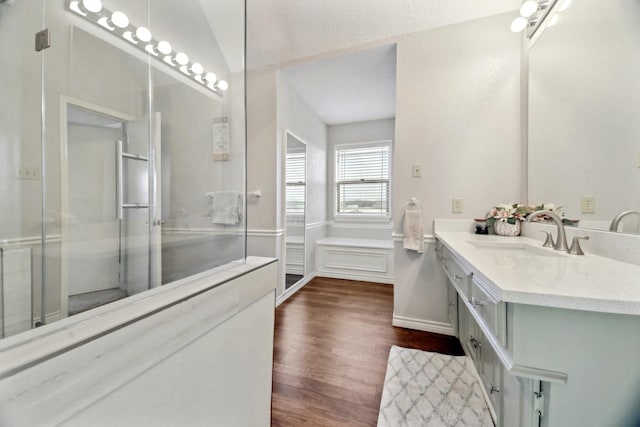 bathroom with a shower with shower door, hardwood / wood-style flooring, a textured ceiling, vaulted ceiling, and vanity