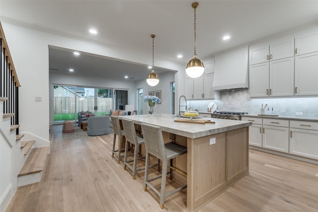 kitchen featuring pendant lighting, premium range hood, white cabinetry, and a center island with sink