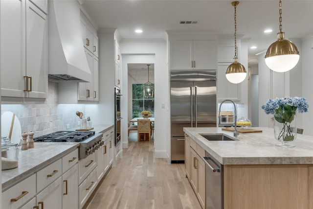 kitchen featuring white cabinets, a center island with sink, custom range hood, and stainless steel appliances