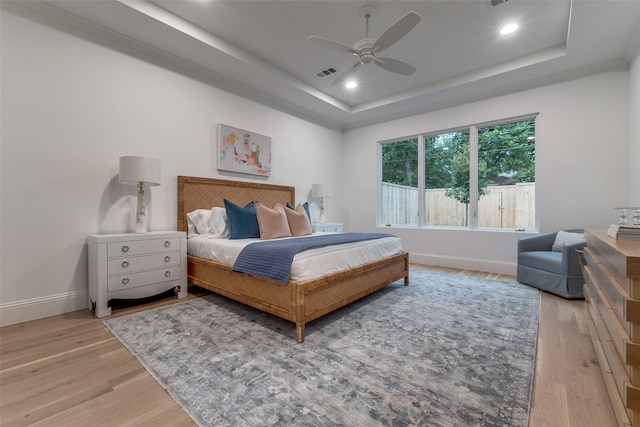 bedroom with ceiling fan, a tray ceiling, and light hardwood / wood-style flooring