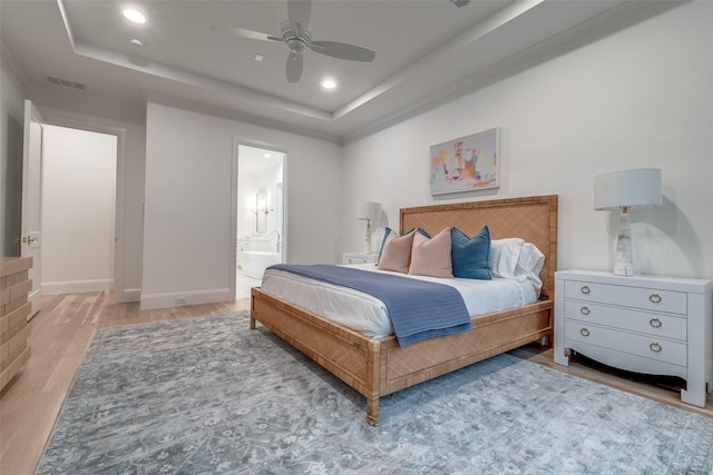 bedroom with ceiling fan, wood-type flooring, a tray ceiling, and ensuite bathroom