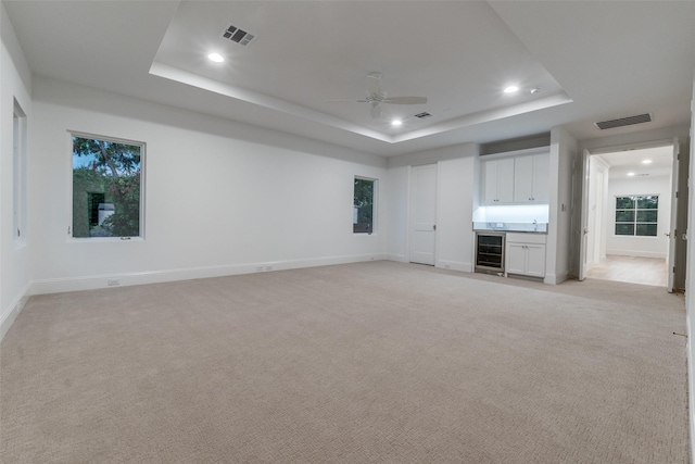 unfurnished living room with beverage cooler, light carpet, indoor bar, a raised ceiling, and ceiling fan