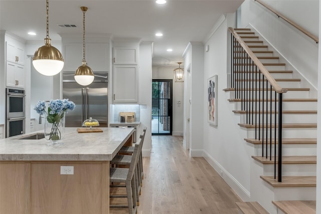 kitchen featuring a center island with sink, appliances with stainless steel finishes, white cabinets, and decorative light fixtures