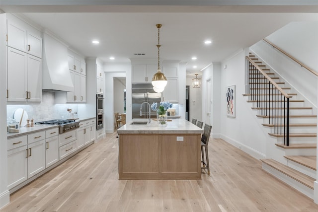 kitchen with white cabinets, a center island with sink, custom range hood, and stainless steel appliances