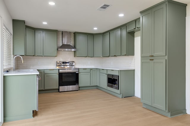 kitchen featuring appliances with stainless steel finishes, wall chimney exhaust hood, green cabinets, and light hardwood / wood-style flooring