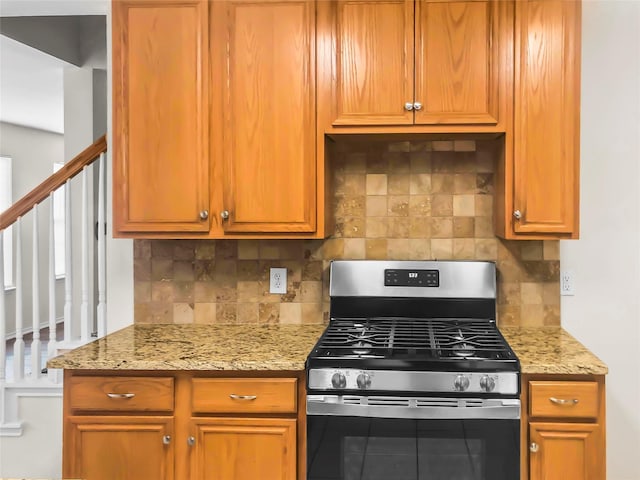 kitchen with stainless steel gas stove, light stone countertops, and backsplash