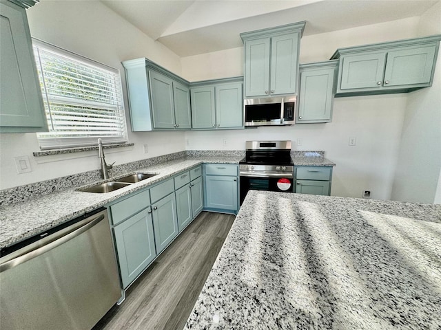 kitchen with light stone countertops, hardwood / wood-style floors, stainless steel appliances, sink, and vaulted ceiling