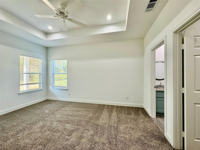 unfurnished room with a raised ceiling, ceiling fan, sink, and dark carpet