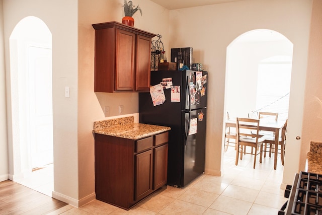 kitchen featuring black refrigerator, light tile patterned floors, and light stone countertops