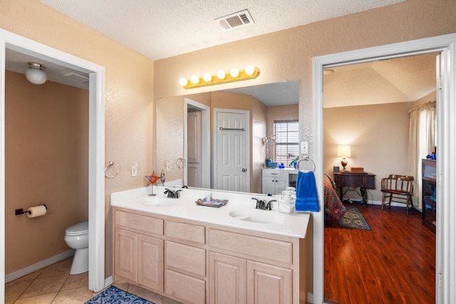 bathroom with toilet, vanity, lofted ceiling, tile patterned floors, and a textured ceiling