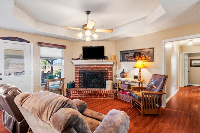 living room with a raised ceiling, ceiling fan, a fireplace, and wood-type flooring