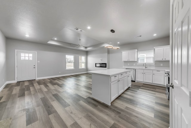 kitchen featuring a center island, a raised ceiling, sink, a textured ceiling, and white cabinets