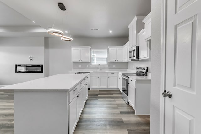 kitchen featuring decorative light fixtures, white cabinets, appliances with stainless steel finishes, and a center island