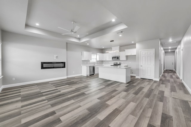 kitchen with stainless steel appliances, a tray ceiling, white cabinetry, and a center island