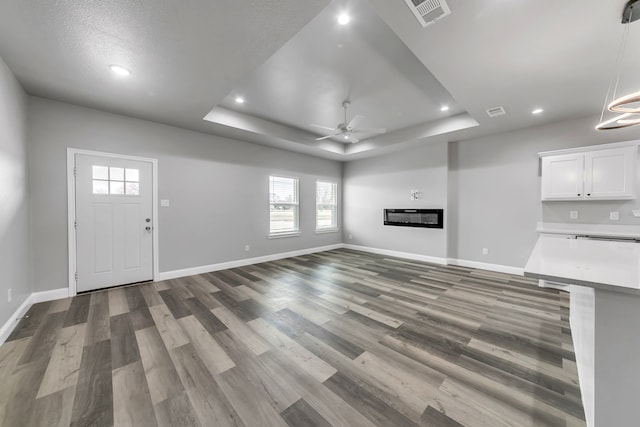 unfurnished living room with a textured ceiling, ceiling fan, wood-type flooring, and a raised ceiling