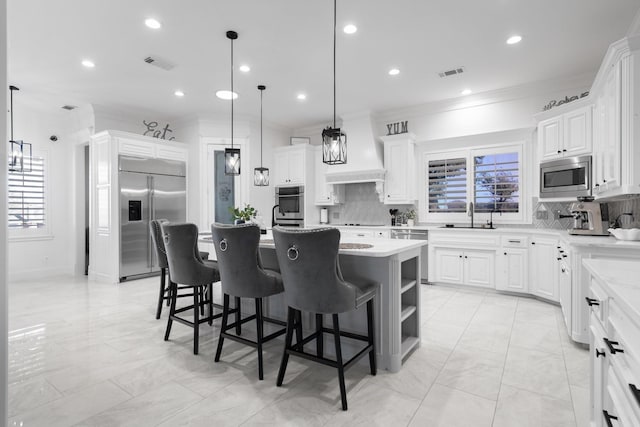 kitchen with pendant lighting, white cabinets, a kitchen island with sink, and built in appliances