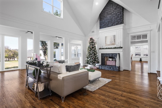 living room with ceiling fan, dark hardwood / wood-style floors, a stone fireplace, and high vaulted ceiling