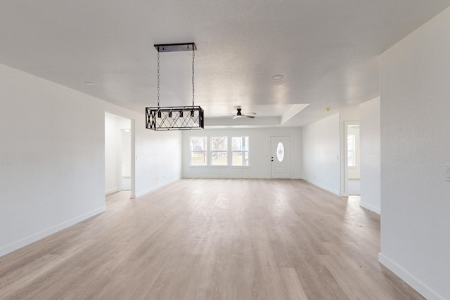 unfurnished living room featuring a raised ceiling, ceiling fan, and light hardwood / wood-style flooring