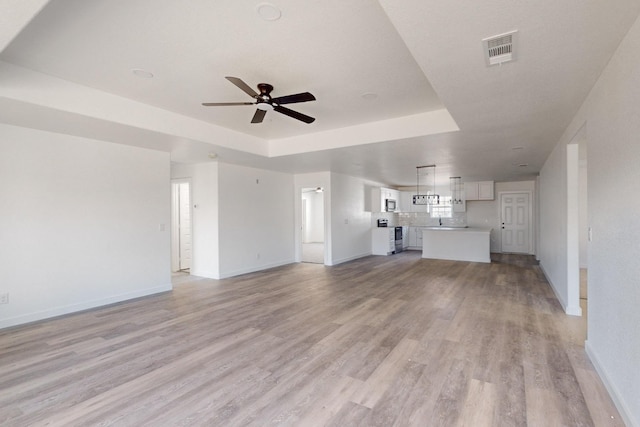 unfurnished living room with ceiling fan, a tray ceiling, and light wood-type flooring