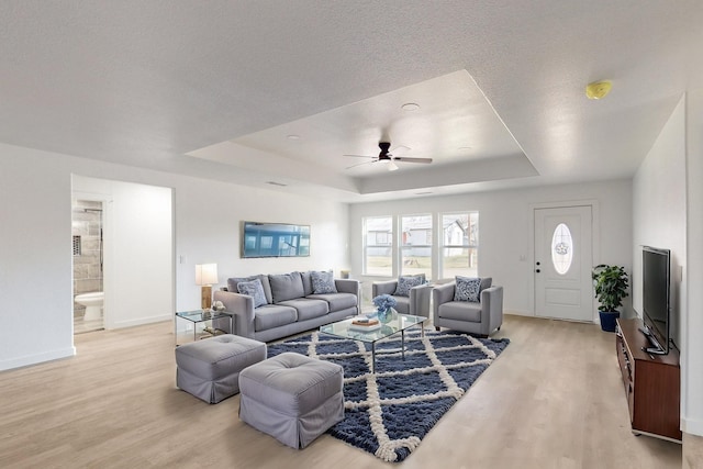 living room with ceiling fan, a tray ceiling, and light wood-type flooring