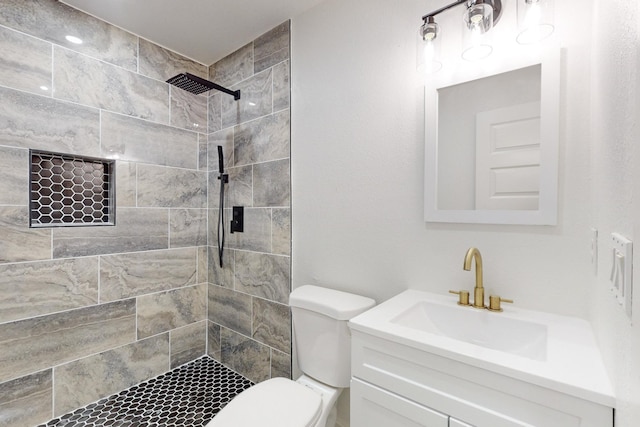 bathroom featuring toilet, tiled shower, and vanity