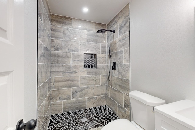 bathroom featuring toilet, vanity, and a tile shower