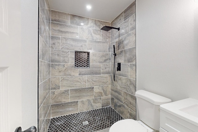 bathroom featuring toilet, a tile shower, and vanity