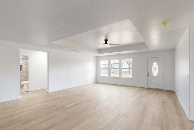 unfurnished living room with ceiling fan, a tray ceiling, and light hardwood / wood-style flooring