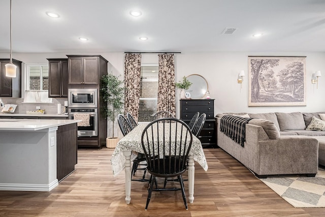 kitchen featuring a center island, decorative light fixtures, stainless steel appliances, light hardwood / wood-style floors, and dark brown cabinets