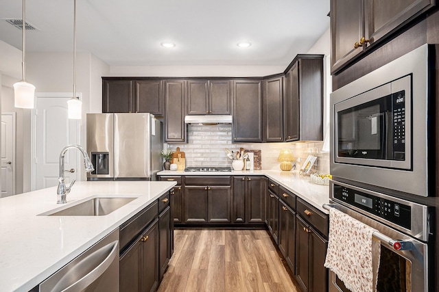 kitchen with pendant lighting, stainless steel appliances, sink, light stone counters, and light hardwood / wood-style flooring