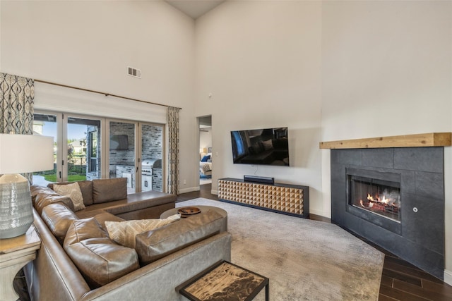 living room featuring a high ceiling, hardwood / wood-style floors, and a tiled fireplace